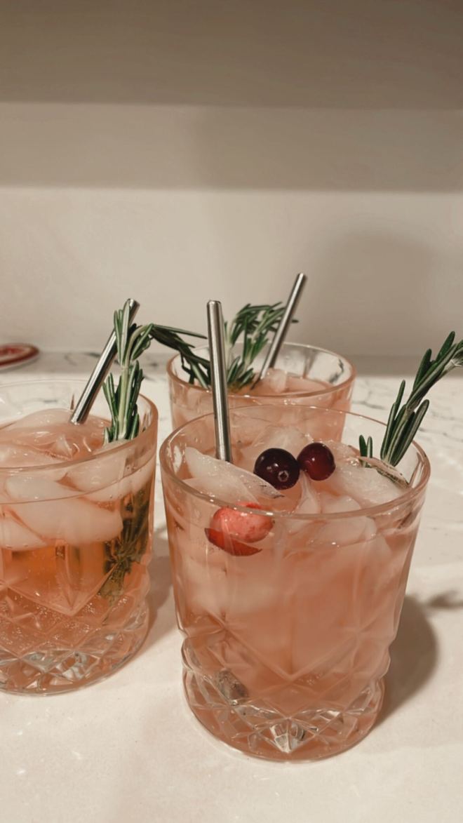 Photo with 3 crystal cocktail glasses filled with a pink cocktail topped off with fresh cranberries and a sprig of rosemary